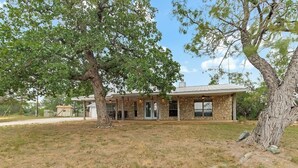A stone house with a covered patio and a garage. - Slab Road Hill Country Escape! (Llano County)