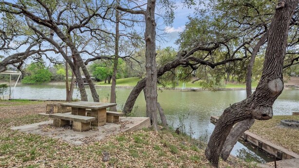 Uma área de piquenique com mesa e bancos à beira de um lago, cercada por árvores.