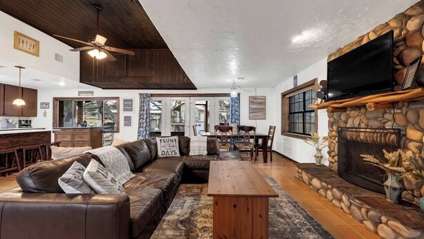 A cozy living room with a leather sofa, wooden coffee table, stone fireplace, and a dining area with a table and chairs. - Lakeside Rock house on Lake LBJ! (Llano County)