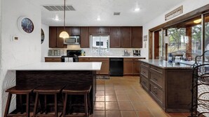 A modern kitchen with a central island, dark wooden cabinets, and a large window. - Lakeside Rock house on Lake LBJ! (Llano County)