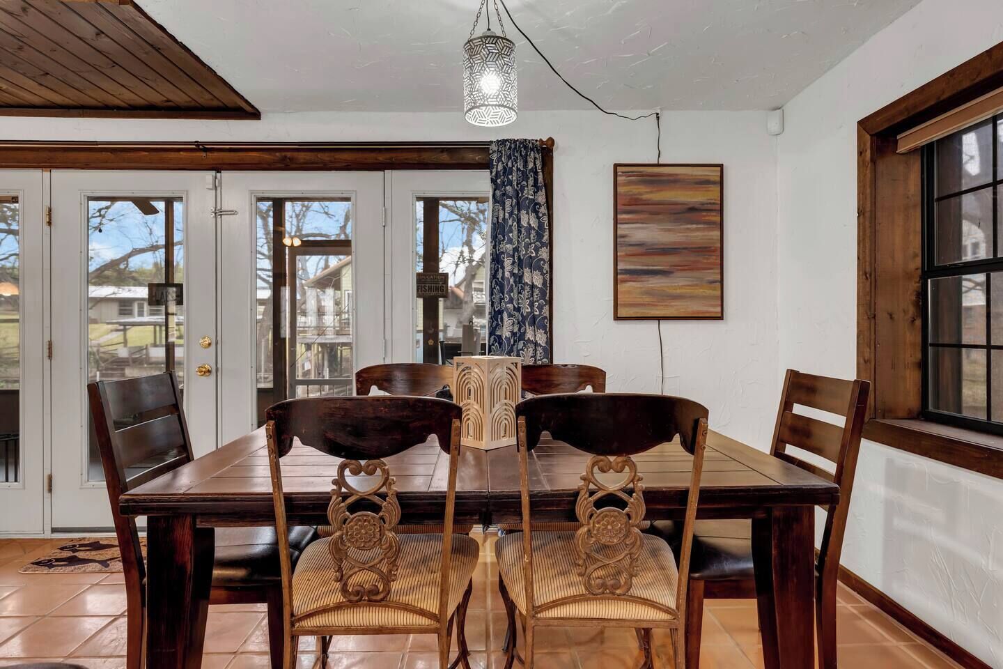 A dining area with a wooden table and chairs, a hanging light fixture, and a view through the glass doors.