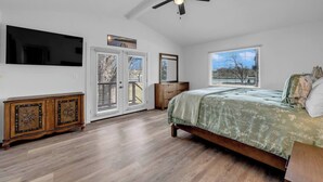 Un dormitorio con cama, ventilador de techo, televisión, cómoda y ventana con vistas.