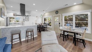A modern kitchen with a central island, dining area with chairs, and large windows offering views of the outdoors. - Lakeside Lounge on Lake LBJ! (Llano County)