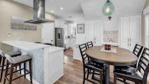 A modern kitchen with white cabinetry, a central island with bar stools, a round dining table, and a hanging light fixture. - Lakeside Lounge on Lake LBJ! (Llano County)