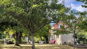 Un espace extérieur verdoyant avec un arbre, un bâtiment doté d’un toit rouge et une clôture en arrière-plan.
