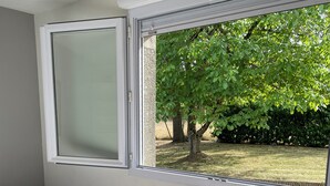 Une chambre à coucher avec un lit, une fenêtre et une vue sur un arbre et de l’herbe.