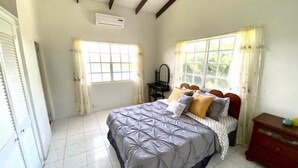 A bedroom with a bed, a dresser, a window with curtains, and an air conditioning unit.