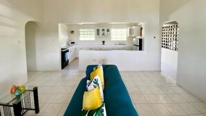 A spacious living area with a sofa, a glass coffee table, and a kitchen in the background.