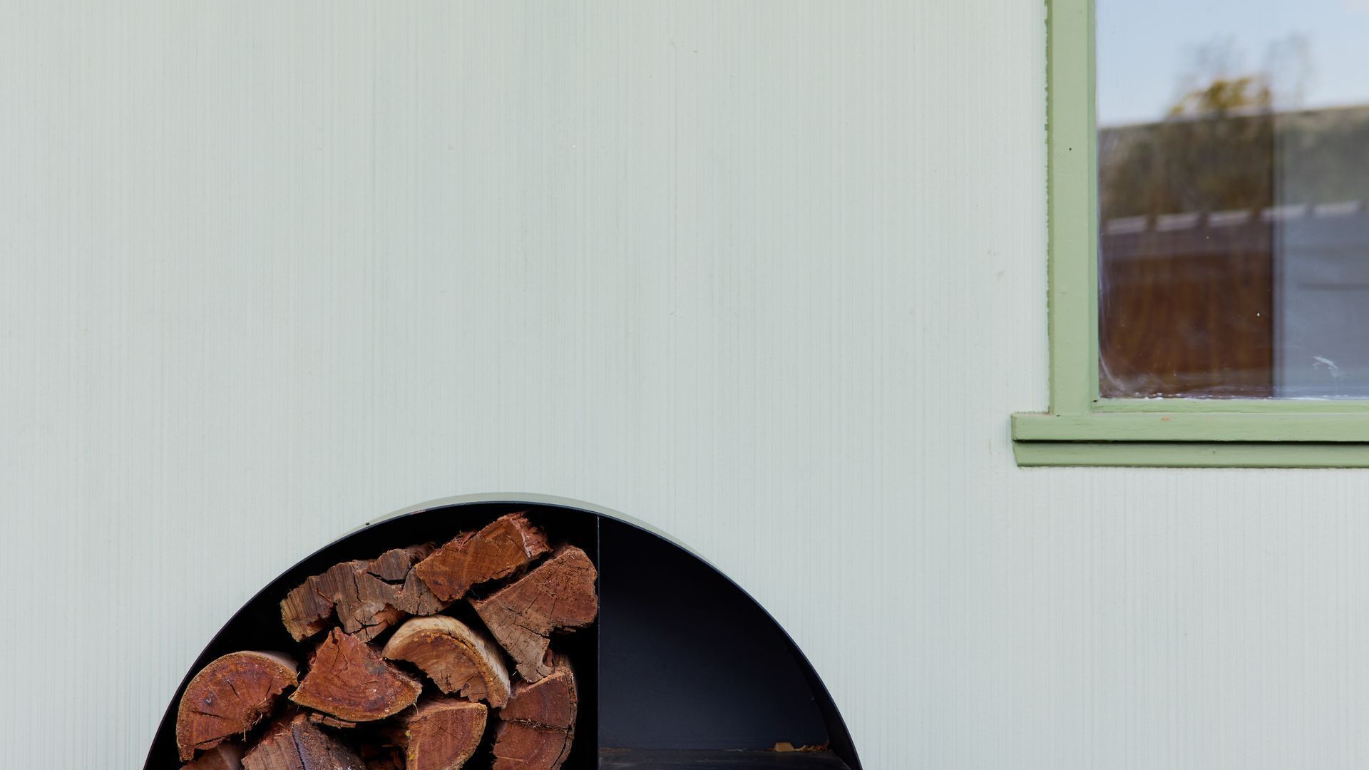 A building exterior with a circular window and a pile of firewood in front.