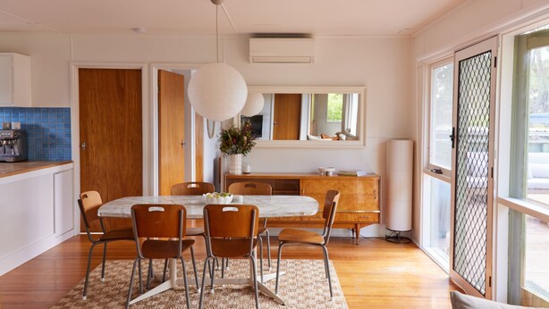 A modern dining area with a marble table, wooden chairs, and a large window with a view. - Lohr Ave Holiday Home (Inverloch)