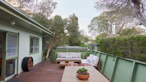 A covered outdoor patio with a wooden table, a sofa, and a potted plant. - Lohr Ave Holiday Home (Inverloch)