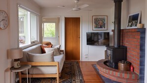 A cozy living room with a sofa, a TV, a fireplace, and a door leading to another room. - Lohr Ave Holiday Home (Inverloch)
