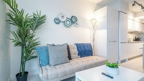 A modern living room with a sofa, a coffee table, a potted plant, and a kitchen in the background. - Spacious 3-bedroom apartment with AC, WiFi in wonderful Vancouver (Vancouver)