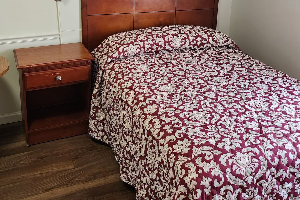 Une chambre à coucher avec une tête de lit en bois, une table de chevet en bois, une couvre-lit à motifs et une lampe fixée au mur.