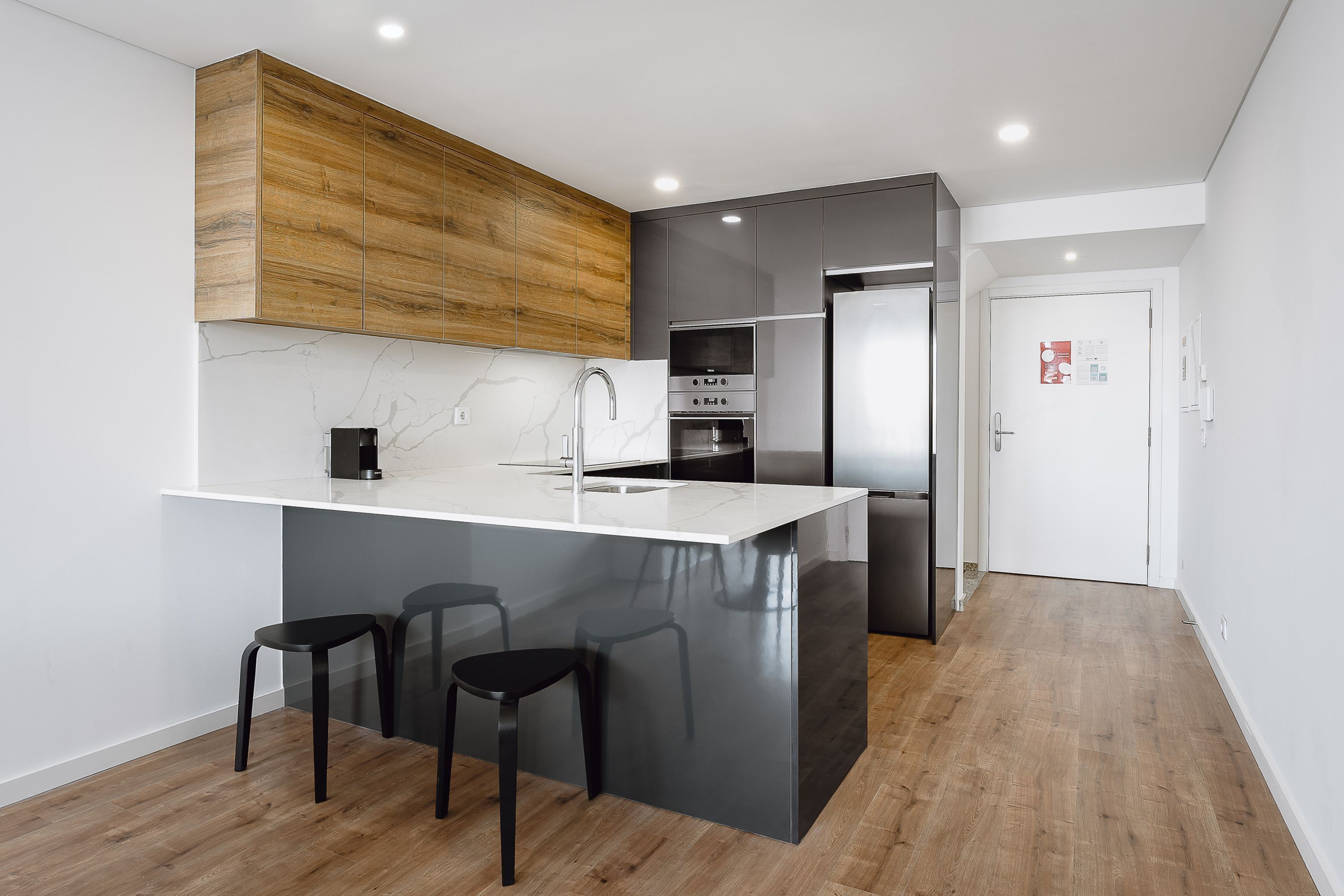 A modern kitchen with a large island, wooden cabinets, stainless steel appliances, and black bar stools.