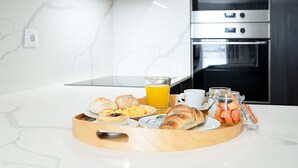 Un plateau de petit-déjeuner avec des viennoiseries, un verre de jus d’orange et une tasse de café, posés sur un plan de travail en marbre dans une cuisine moderne équipée d’appareils électroménagers en acier inoxydable.