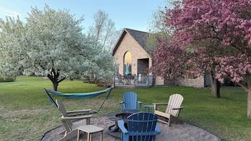 Un espace extérieur aménagé avec un hamac, des fauteuils Adirondack et un foyer.