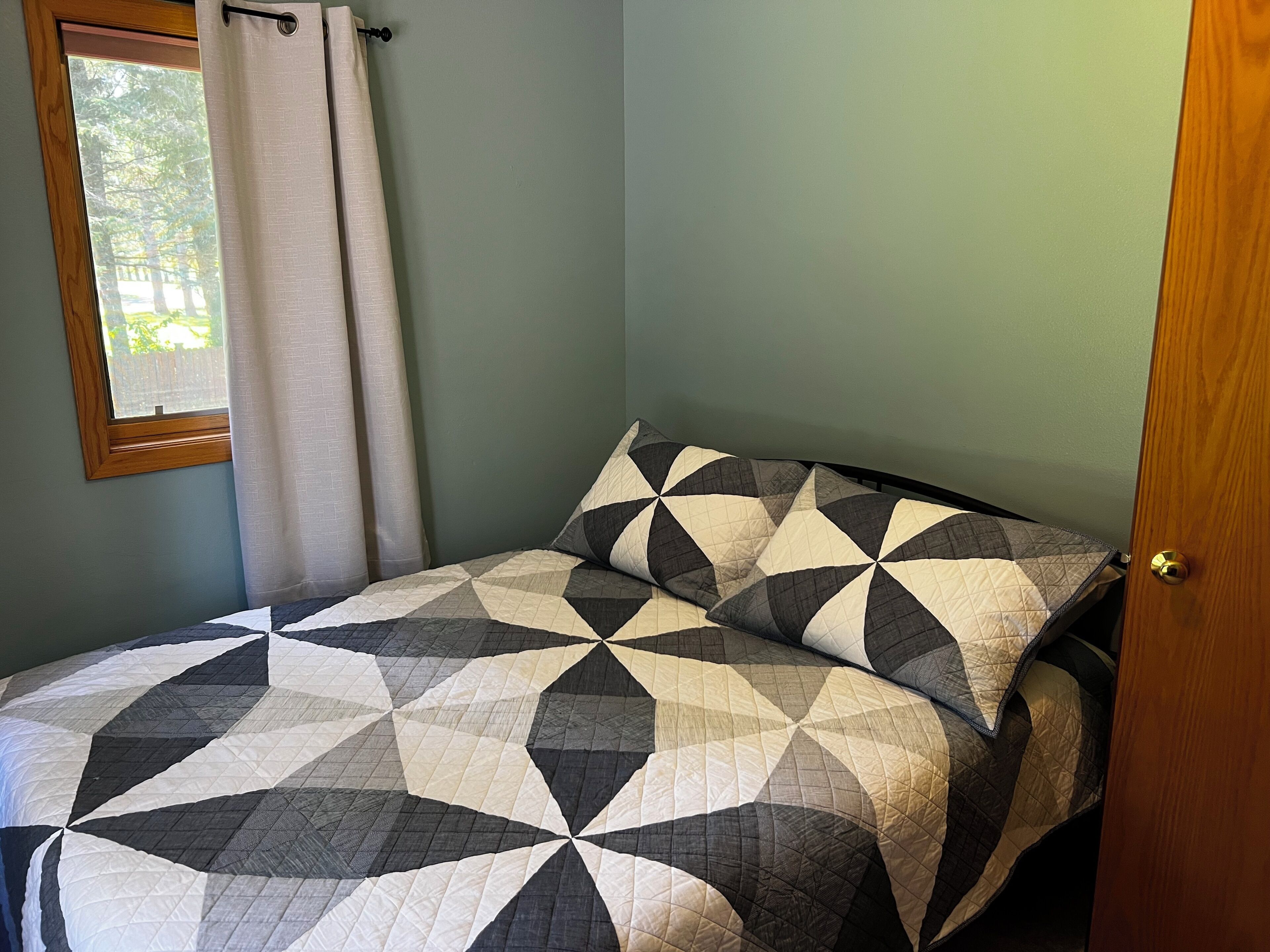 A bedroom with a bed, a window with curtains, and a door.