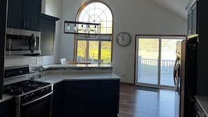 A kitchen with a large island, dark cabinets, stainless steel appliances, and a large window with a view of the outdoors. - The Fairway Escape – Spacious 6BR Golf Course Retreat, Walk to Downtown Hayward! (Hayward)