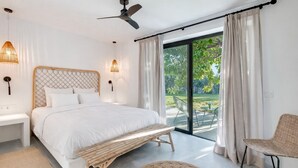 Une chambre à coucher avec un lit, des tables de chevet, un ventilateur de plafond et une vue sur l’extérieur.