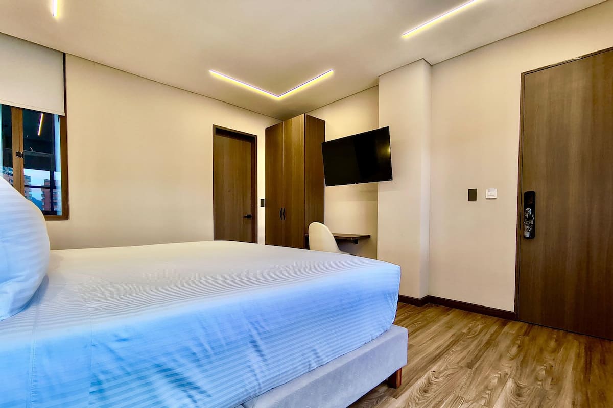 Una habitación de hotel moderna con una cama grande, un armario de madera, un televisor de pantalla plana y piso de madera.