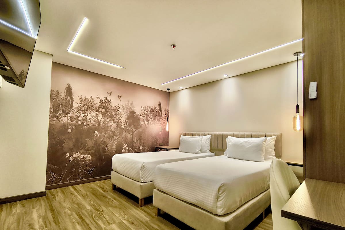 Una habitación de hotel moderna con dos camas, piso de madera, un mural y un escritorio con lámpara.