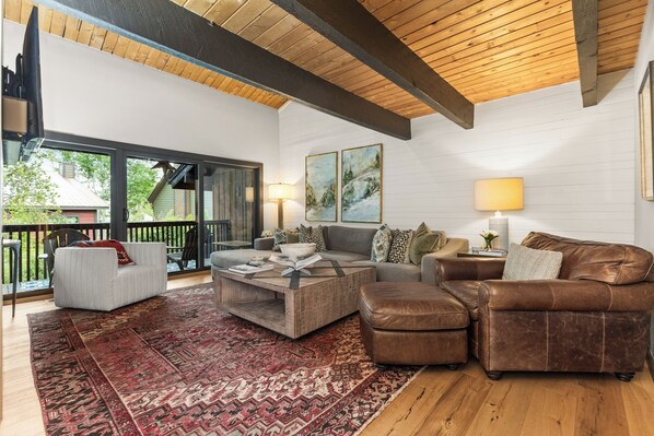 A spacious living room with a large window, a wooden ceiling, and a red patterned rug. - Steps to Bus Stop|Private Hot Tub|A/C in Upper Bedroom (Steamboat Springs)
