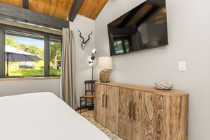 A bedroom with a bed, wooden headboard, a TV mounted on the wall, a desk with a lamp, and a window with a view of the outdoors. - Steps to Bus Stop|Private Hot Tub|A/C in Upper Bedroom (Steamboat Springs)