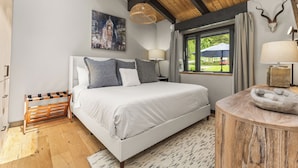 Una camera da letto con un letto, un comodino, una lampada, una finestra con tende, una panca in legno e un'opera d'arte appesa al muro.