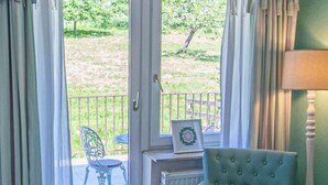 A room with a teal armchair, a small table with a tray, a radiator, and a view of an outdoor patio with a chair and a fence.