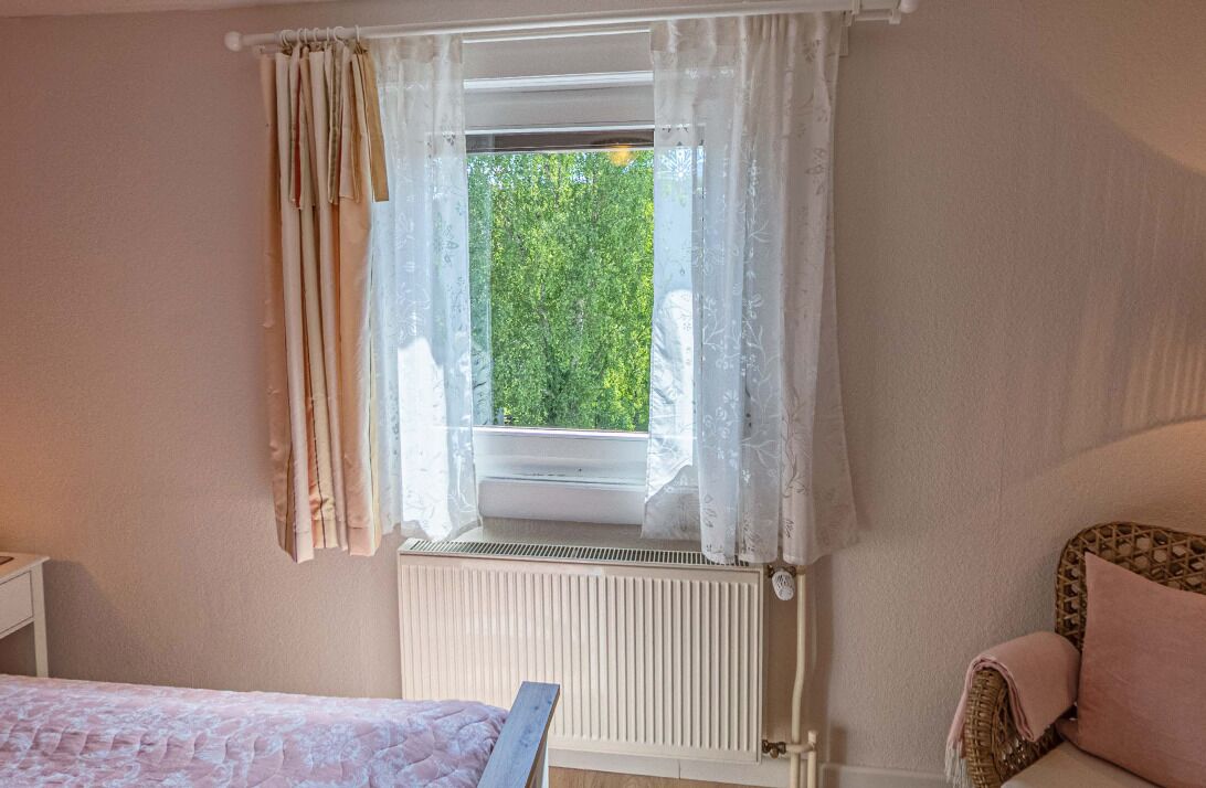 A bedroom with a window, a radiator, a bed, and a chair.