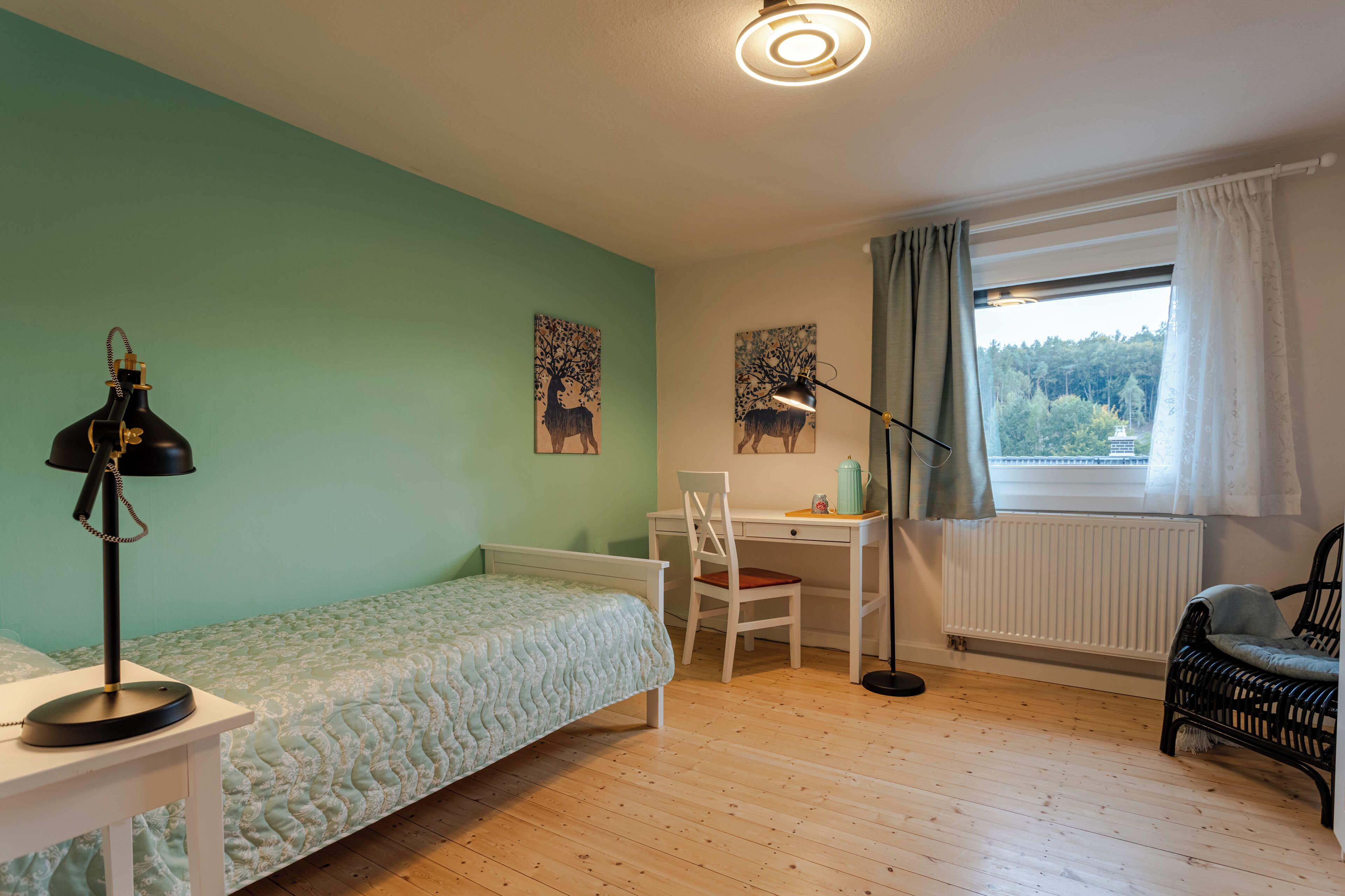 A bedroom with a bed, desk, chair, and a window with curtains.