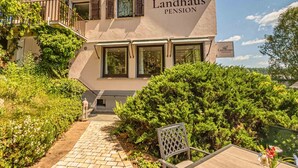 A building with the sign "Landhaus Pension" and a pathway leading to a table and chair.