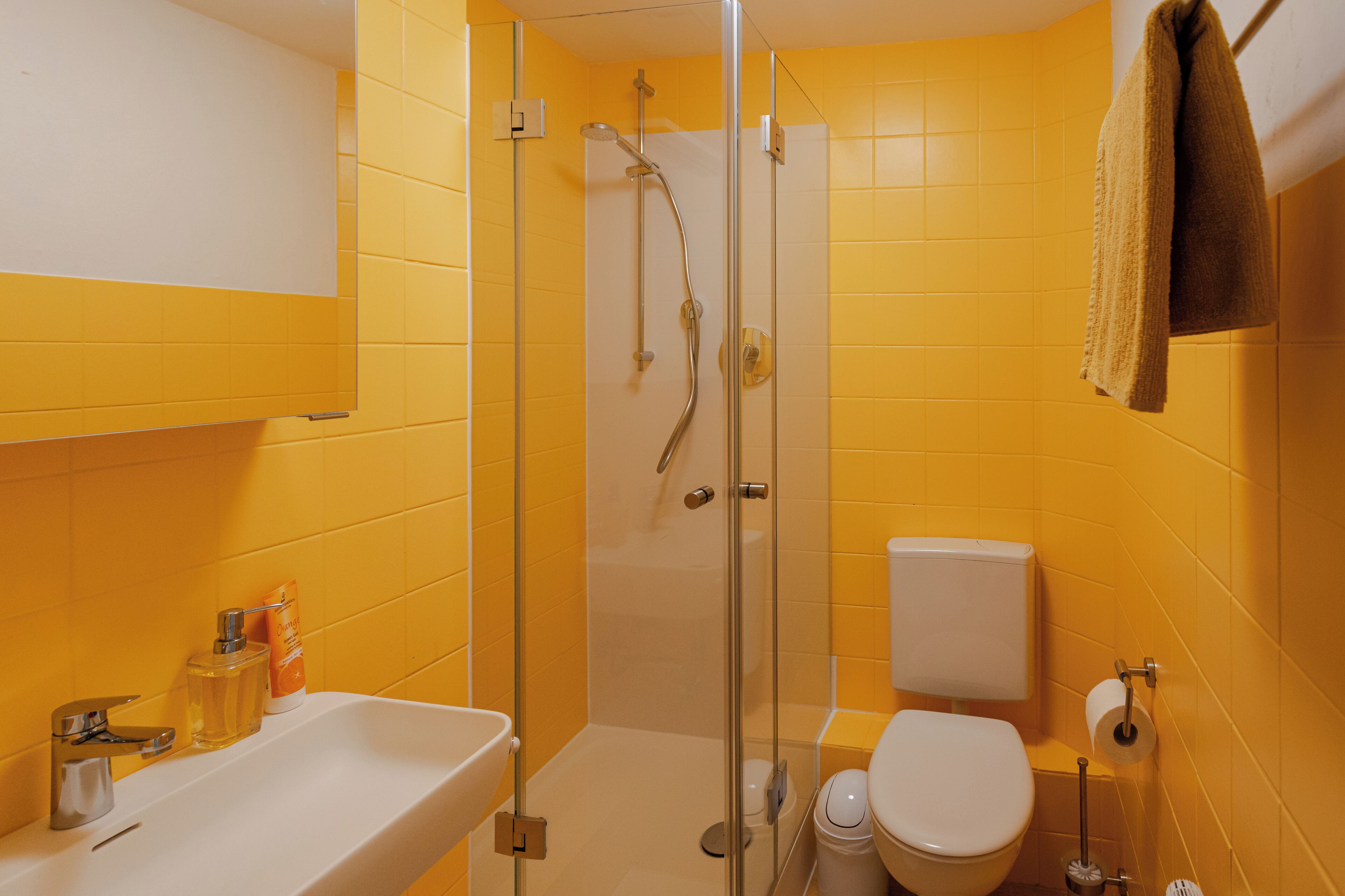 A bathroom with yellow walls, a glass-enclosed shower, a white sink, and a toilet.