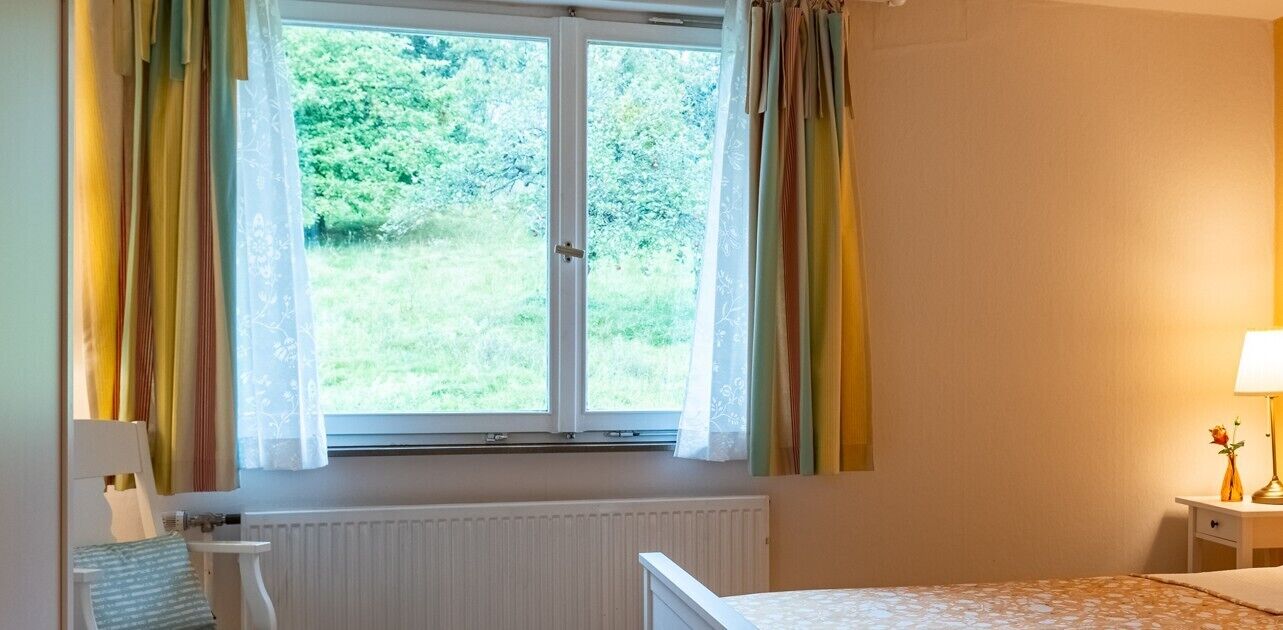 Ein Schlafzimmer mit Fenster, Heizkörper, Nachttisch und Lampe.