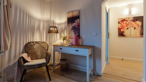 A room with a wicker chair, a white desk with drawers, a floor lamp, and a painting on the wall.