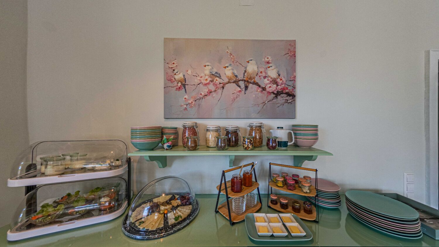 Ein reichhaltiges Buffet mit verschiedenen Speisen, Glasbehältern und einem Gemälde von Vögeln auf einem Ast.