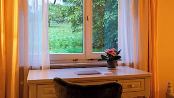 Quarto com escrivaninha e cadeira, janela com cortinas e uma planta em vaso no parapeito.