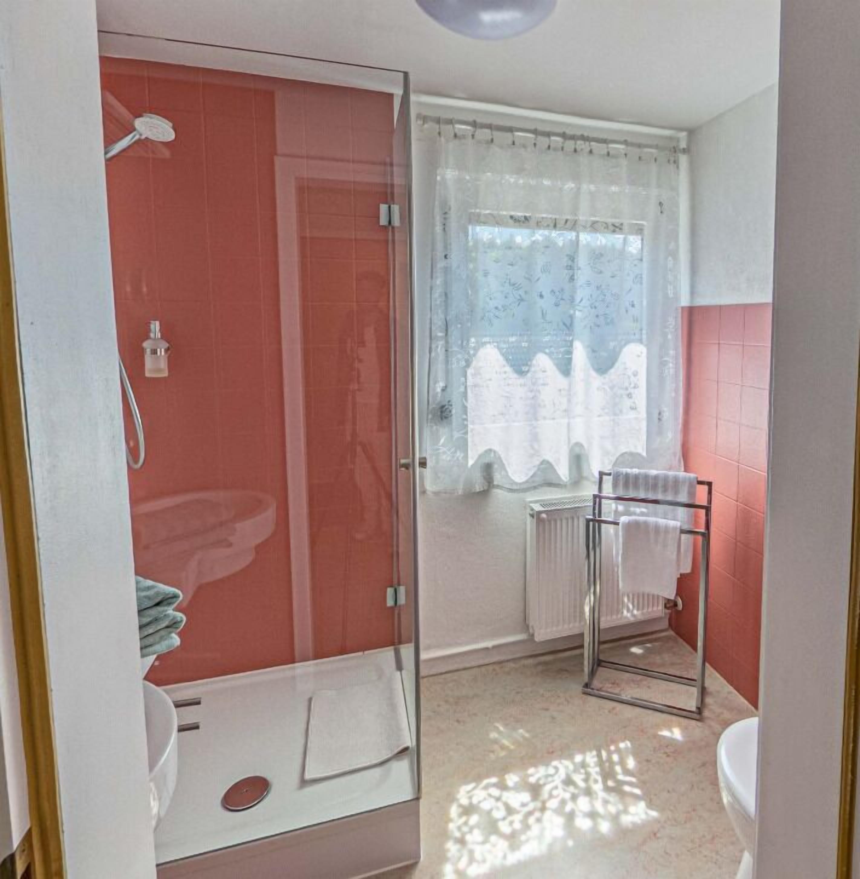 Un baño con cabina de ducha de vidrio, un lavabo blanco, un inodoro y un perchero para toallas.