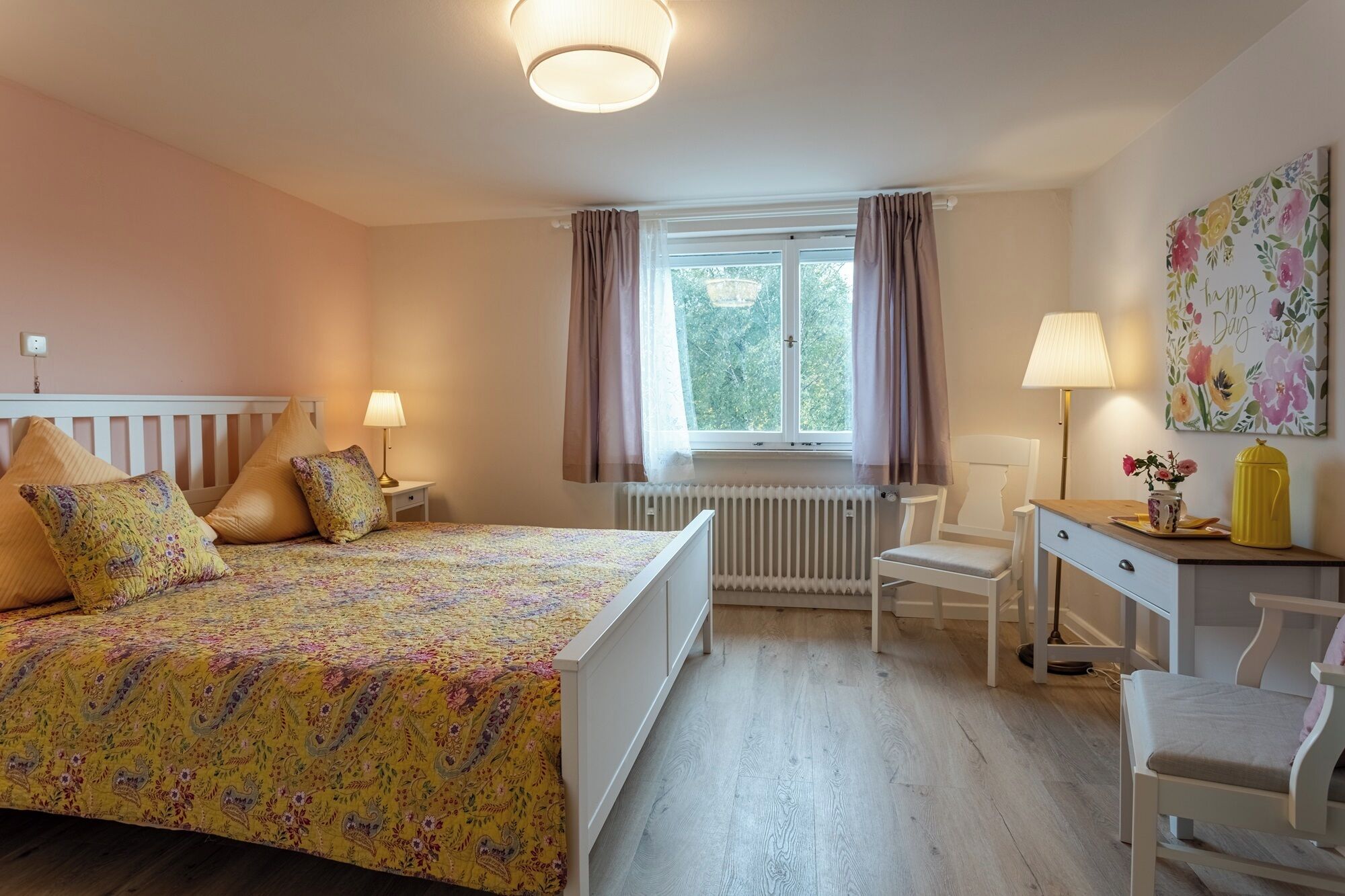 Een slaapkamer met een bed, een bureau, een stoel, een radiator en een raam met gordijnen.