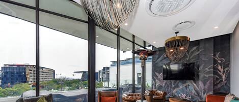 A modern lounge with leather chairs, a fireplace, and large windows offering city views.
