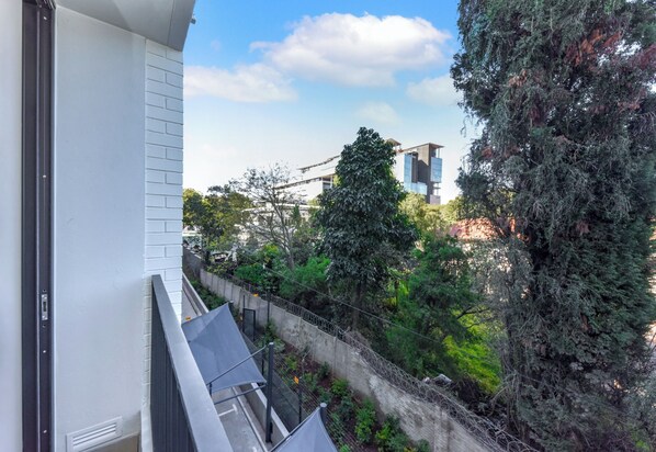 A balcony with a view of a tree-lined street and a building in the background.
