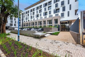 A modern hotel with a clean, white facade, a well-maintained outdoor area with a paved walkway, and a parking lot.
