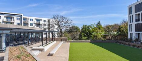 A modern building with a glass facade, a green lawn, and a clear sky.