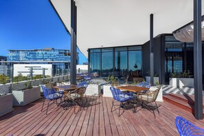 A rooftop terrace with wooden flooring, blue wicker chairs, and a wooden table.