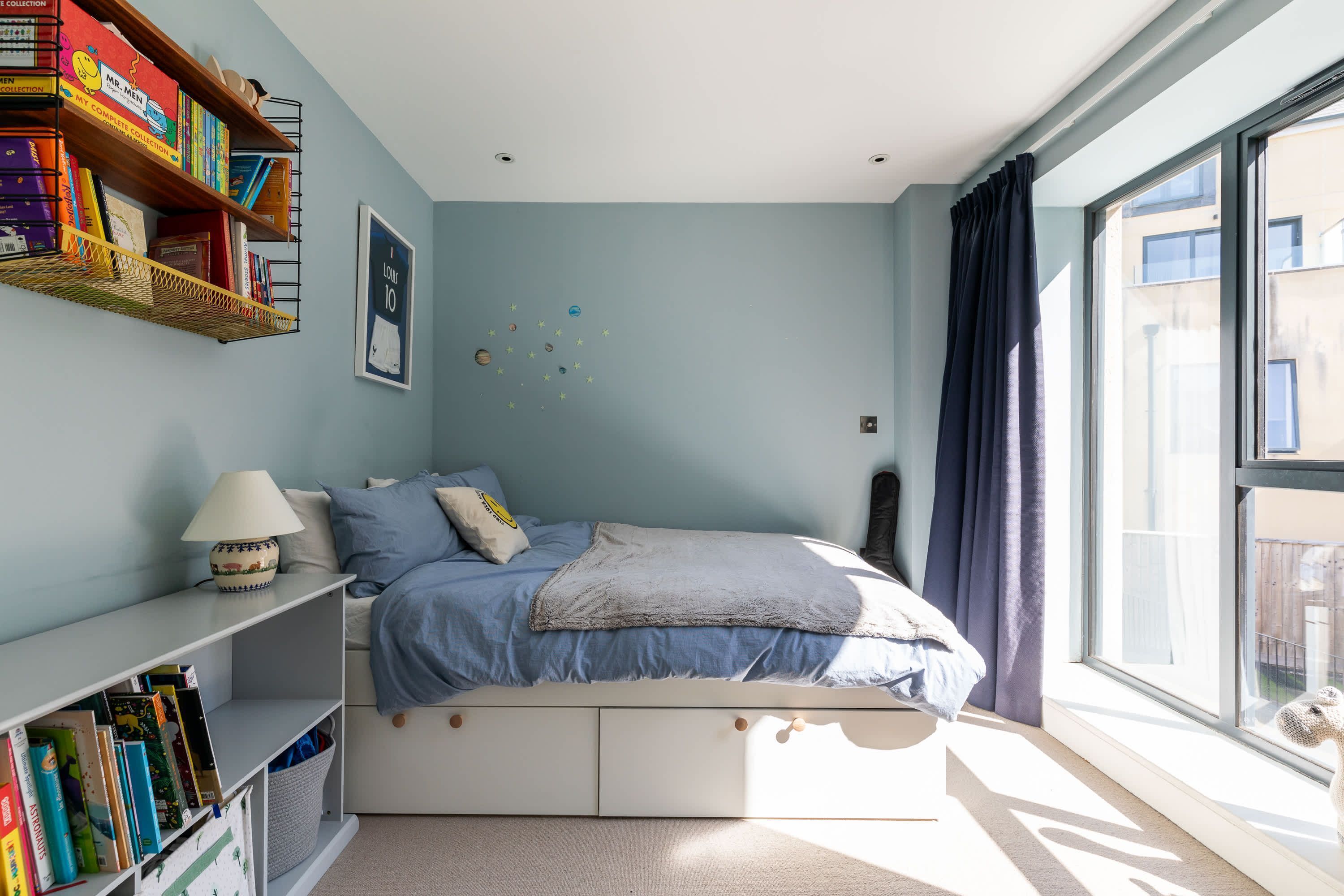 Une chambre à coucher avec un lit, des étagères, une fenêtre et un élément décoratif mural.