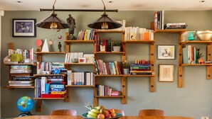 A room with a wooden dining table, chairs, and a globe on the table. Shelves with books and decorative items line the walls.