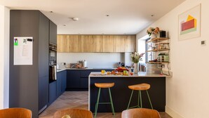 A modern kitchen with wooden cabinets, a central island with stools, and a dining area with a fruit bowl.