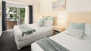 Habitación de hotel con dos camas, un balcón con cortinas, un ventilador de techo y un cuadro en la pared.