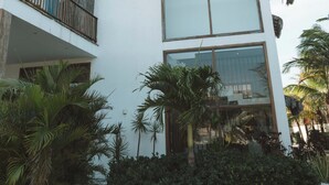 Un bâtiment moderne à deux étages, doté d’une façade blanche, de grandes fenêtres et d’un balcon surmonté d’un toit de chaume.